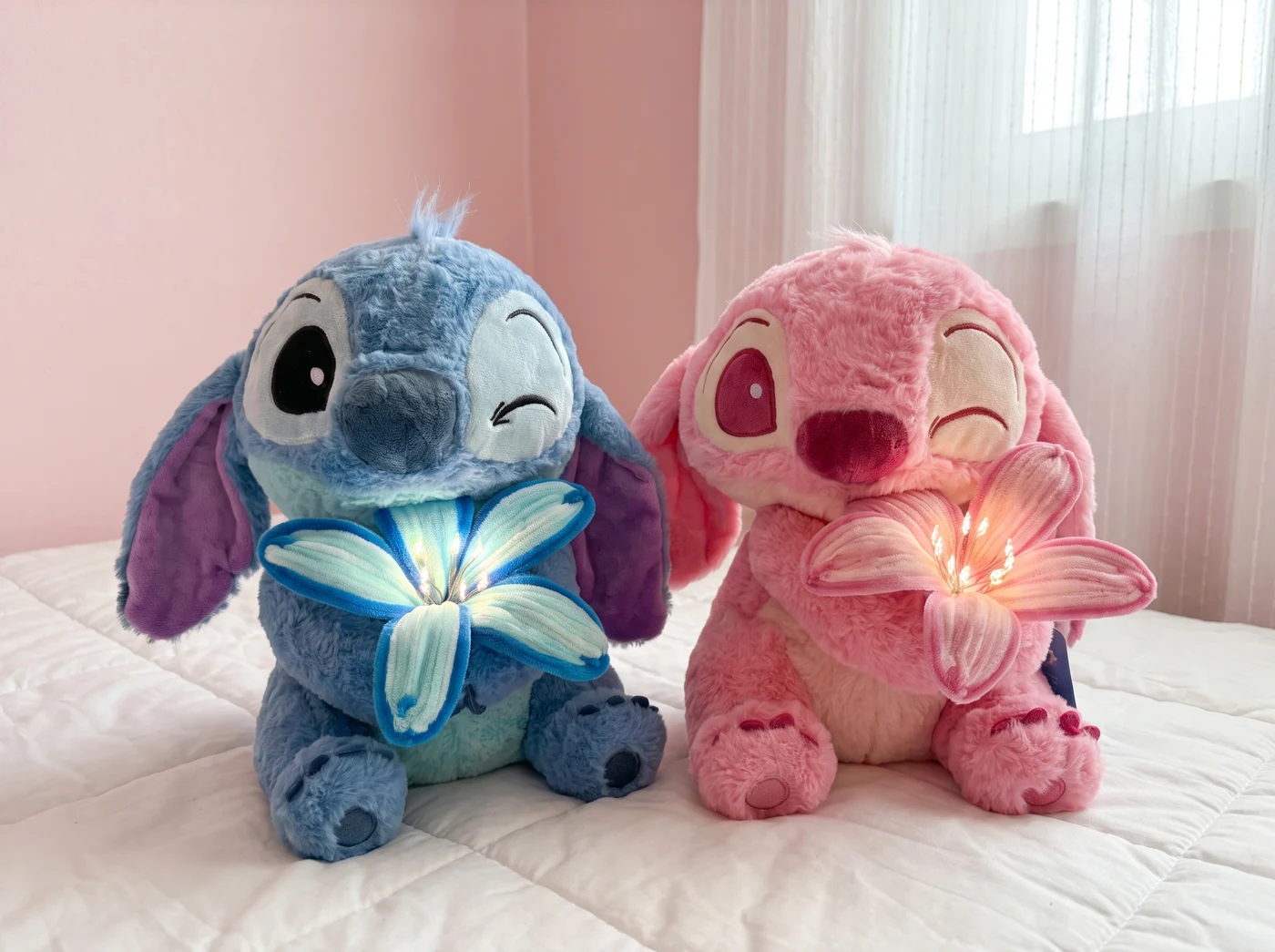 Pink and blue flower plushies sitting together on a white bed